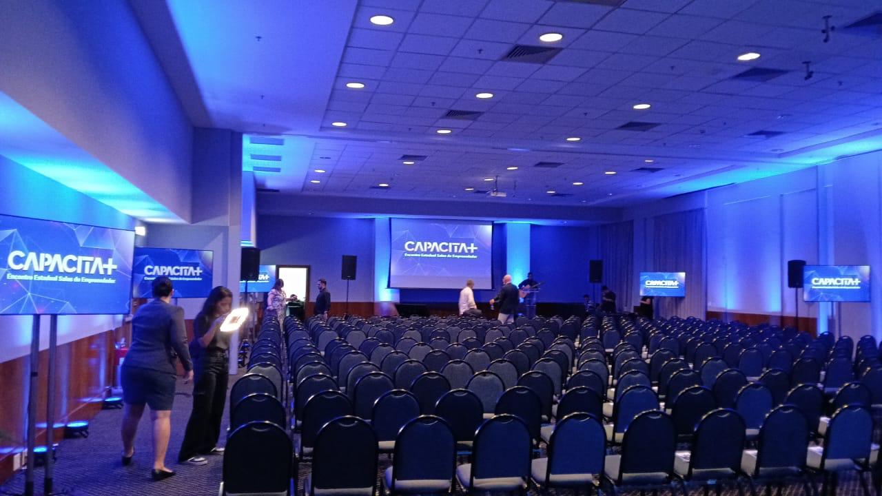 Auditório Capacita+ preparado com telas, cadeiras e iluminação azul